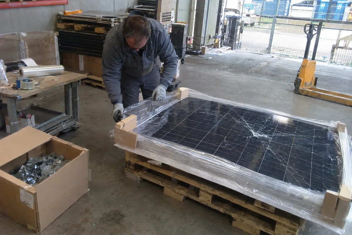 Eine Fachkraft verpackt ein beschädigtes Solarmodul flach auf einer gepolsterten Palette mit geschützten Kanten.
